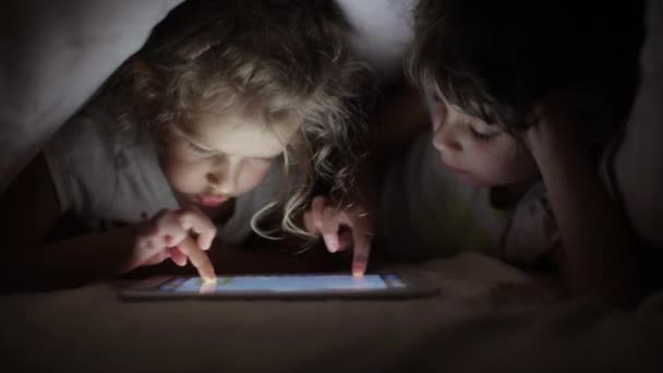 Deux petites filles sœurs dessinent sur une tablette PC se cachant sous une couverture — Video
