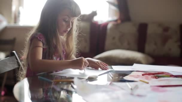 Маленька дівчинка малює з олівцями, сидячи за столом — стокове відео