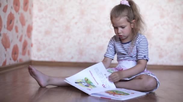 Lilla flickan läsa en bok liggande på golvet — Stockvideo