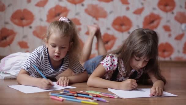 Kleine Zwillingsschwestern zeichnen auf Papier mit Buntstiften, die auf dem Boden liegen. — Stockvideo