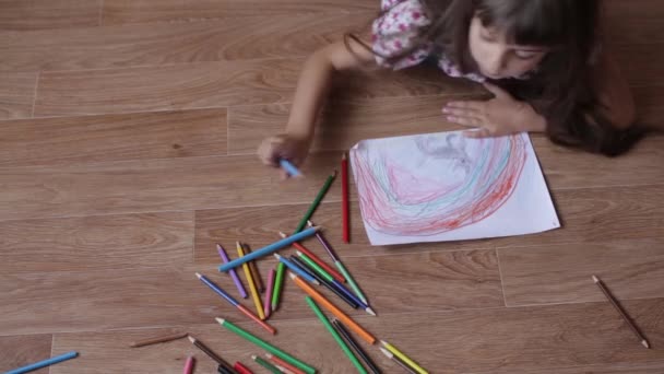 Молоді сестри близнюки малюють на папері з кольоровими олівцями, що лежать на підлозі . — стокове відео