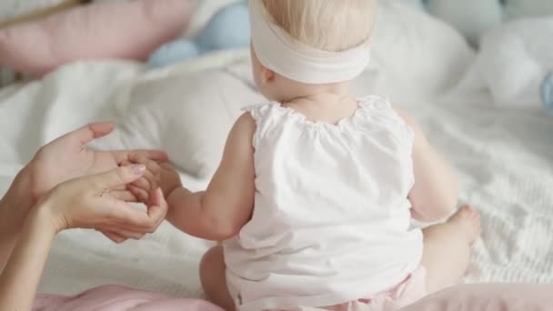 Close-up portret van een klein kind in een licht pak van achteren. Moeders zachte handen houden de kleine hand van de baby vast. Moeder en dochter samen — Stockvideo