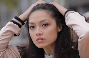 Genç Asyalı kadın kentsel alanda kameraya poz veriyor. İnsanlar fotoğraf çekiyor.