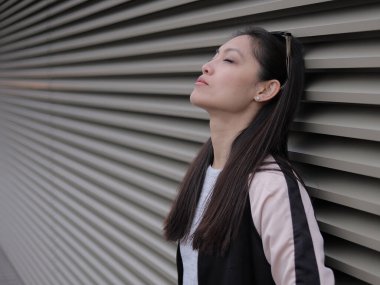 Genç Asyalı kadın kentsel alanda kameraya poz veriyor. İnsanlar fotoğraf çekiyor.