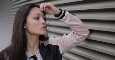 Genç Asyalı kadın kentsel alanda kameraya poz veriyor. İnsanlar fotoğraf çekiyor.