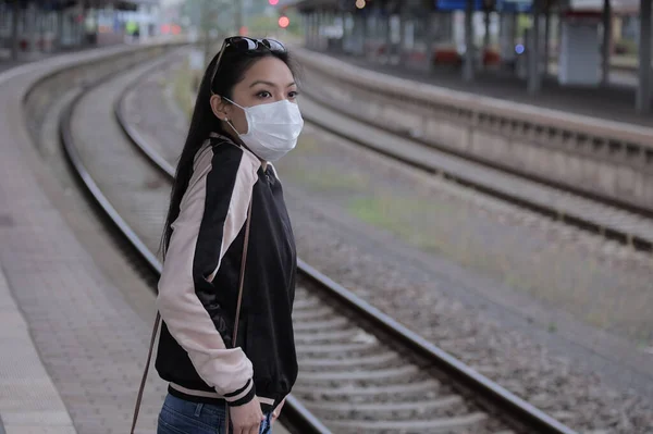 Young woman with a face mask waits for the train