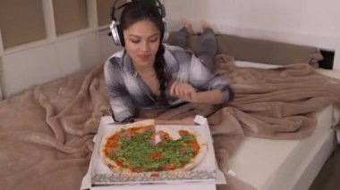 Yatağa uzanmış pizza yiyen genç bir kadın.