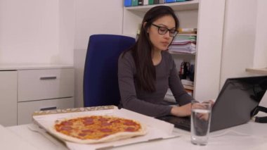Genç bir kadın işteyken teslimat servisinden pizza yiyor.