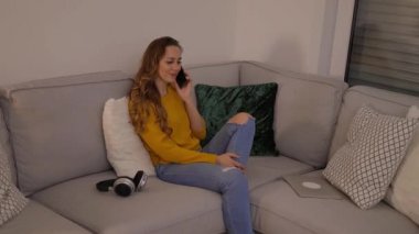 Genç ve rahat bir kadın telefonda kanepede oturuyor.
