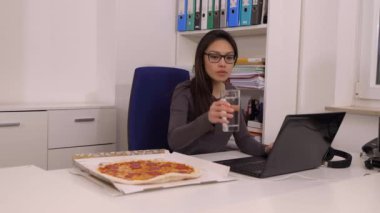 Genç bir kadın işteyken teslimat servisinden pizza yiyor.