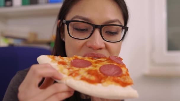 Молодая женщина ест пиццу из службы доставки во время работы — стоковое видео