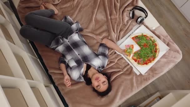 Jovem mulher bonita deita-se na cama e come pizza — Vídeo de Stock