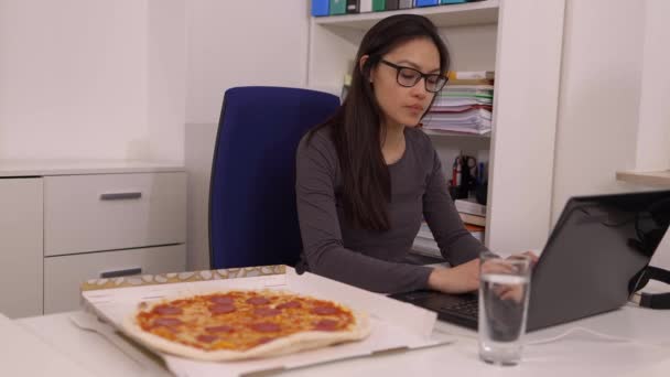 Молода жінка їсть піцу з служби доставки під час роботи — стокове відео