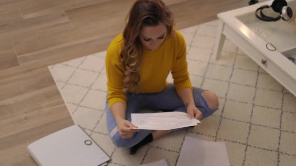 Молода жінка сидить на підлозі і сортує документи — стокове відео