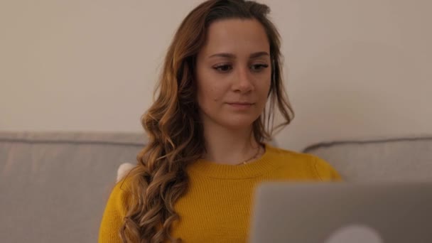 Молода жінка сидить на дивані зі своїм ноутбуком — стокове відео