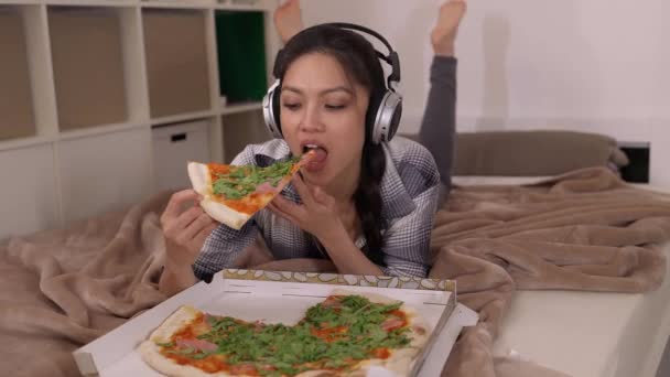 Молодая женщина лежит на кровати и ест пиццу. — стоковое видео