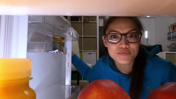 Молодая женщина ищет еду и напитки в холодильнике — стоковое видео