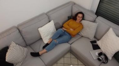 Genç bir kadın kanepede uzanıyor ve televizyon izliyor.