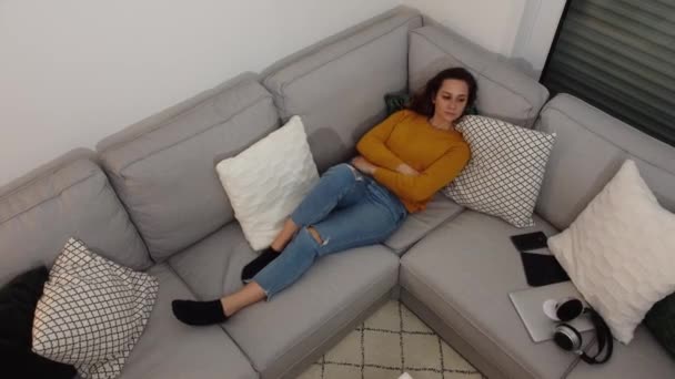 Молодая женщина лежит на диване и смотрит телевизор — стоковое видео