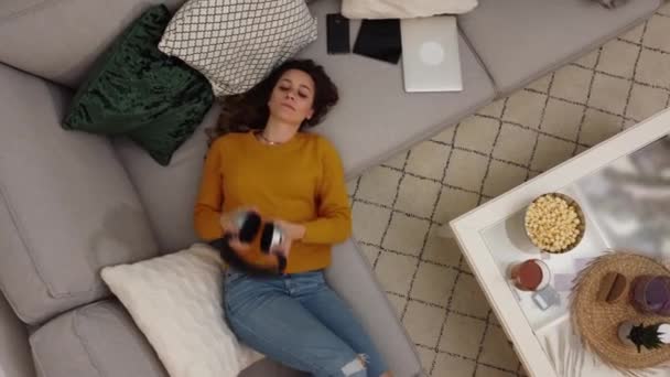 Wanita muda berbaring di sofa mendengarkan musik — Stok Video