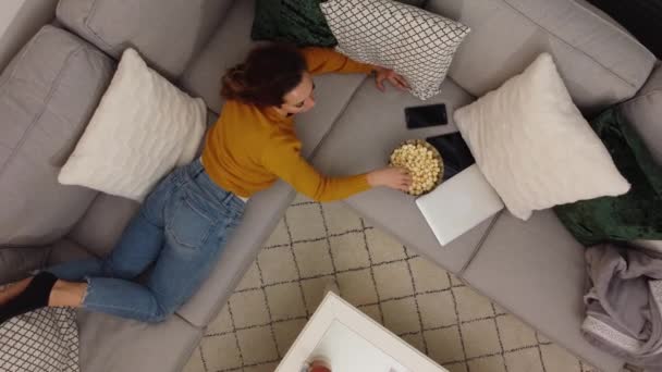 Молода жінка лежить на дивані і дивиться телевізор — стокове відео