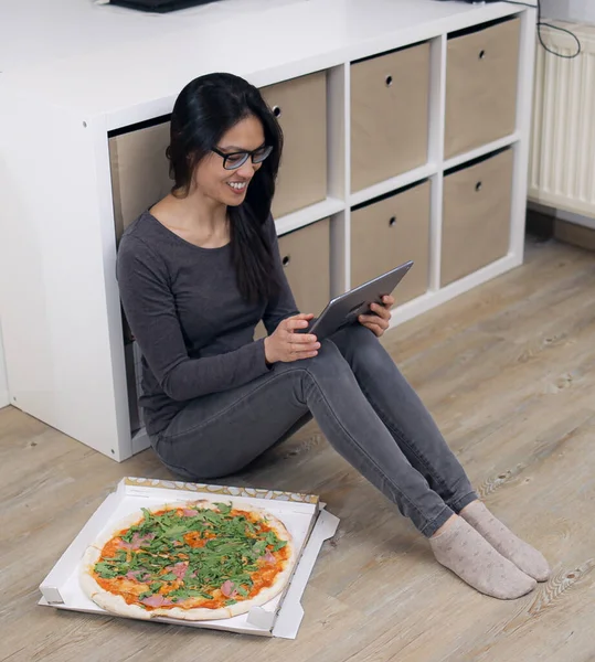年轻的女人和她的平板电脑坐在地板上吃披萨 — 图库照片