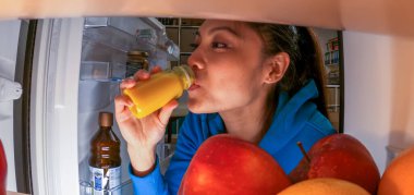 Genç bayan buzdolabından nefis bir meyve suyu alıyor.