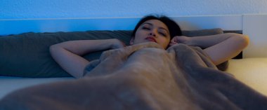Genç Asyalı kadın yatakta yatarken uyanıyor.