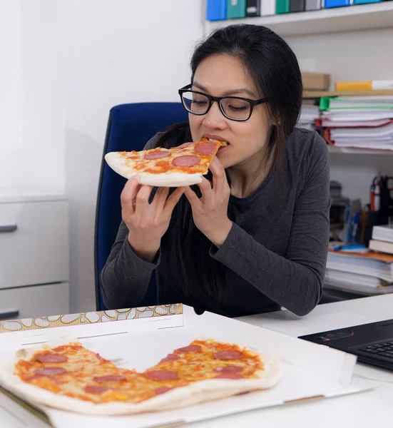 Молодая женщина ест пиццу из службы доставки во время работы — стоковое фото