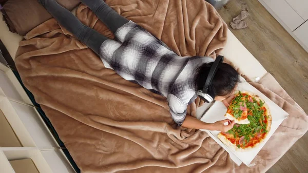 Mladá hezká žena leží na posteli a jí pizzu — Stock fotografie