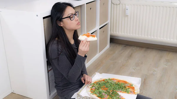 Młoda kobieta siedzi na podłodze i je pizzę. — Zdjęcie stockowe