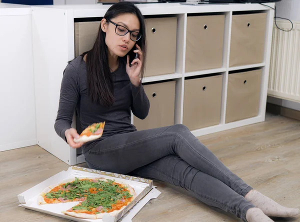 Молодая женщина отвечает на телефонный звонок во время еды пиццы — стоковое фото