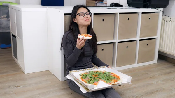 Młoda kobieta siedzi na podłodze i je pizzę. — Zdjęcie stockowe