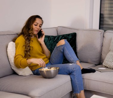 Genç ve rahat bir kadın telefonda kanepede oturuyor.