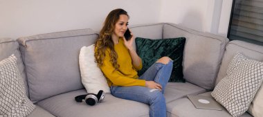 Genç ve rahat bir kadın telefonda kanepede oturuyor.