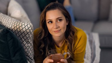 Genç güzel bayan kanepede yatarken bir fincan çay içer.