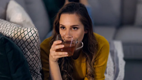 Молодая красивая женщина пьет чашку чая, лежа на диване — стоковое фото