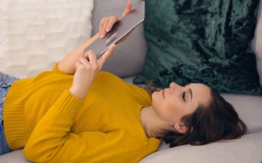 Kanepede tablet bilgisayarı olan genç bir kadın.