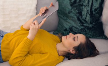 Kanepede tablet bilgisayarı olan genç bir kadın.