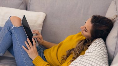 Kanepede tablet bilgisayarı olan genç bir kadın.