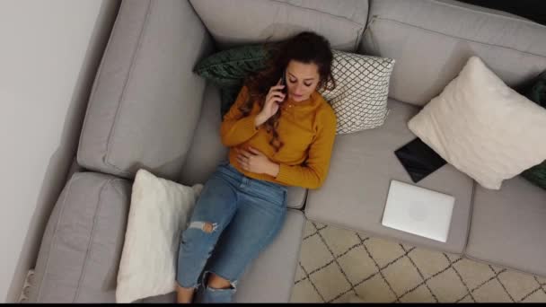 Mujer joven se sienta en el sofá y hace llamadas telefónicas — Vídeos de Stock