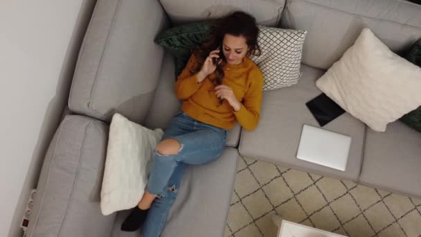 Mujer joven se sienta en el sofá y hace llamadas telefónicas — Vídeo de stock