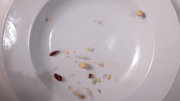 Сніданок Зернові та сухофрукти падають на тарілку в повільному русі — стокове відео