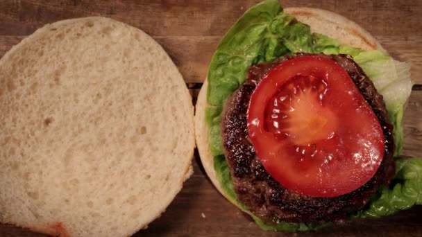 Hamburger dengan salad, daging panggang dan tomat di atas roti burger — Stok Video