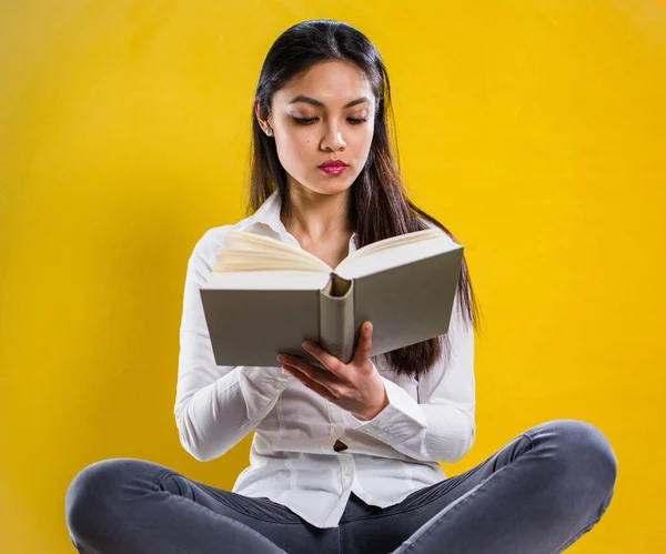 Kitap okuyan genç bir kadın - sarı arka planda stüdyo çekimi — Stok fotoğraf