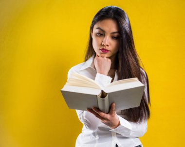 Kitap okuyan genç bir kadın - sarı arka planda stüdyo çekimi