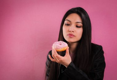 Genç bir kadın pembe arka planda donut yiyor.