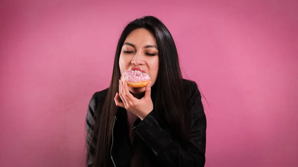 Νεαρή γυναίκα τρώει ντόνατ σε ροζ φόντο — Φωτογραφία Αρχείου
