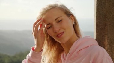 Genç sarışın kadın rüzgarlı bir günde kameraya gülümser. İnsanlar ağır çekimde fotoğraf çeker.