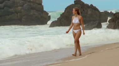 Bikini giyen seksi bir kadın okyanusta kumlu bir sahilde yürüyor - aşırı yavaş çekim
